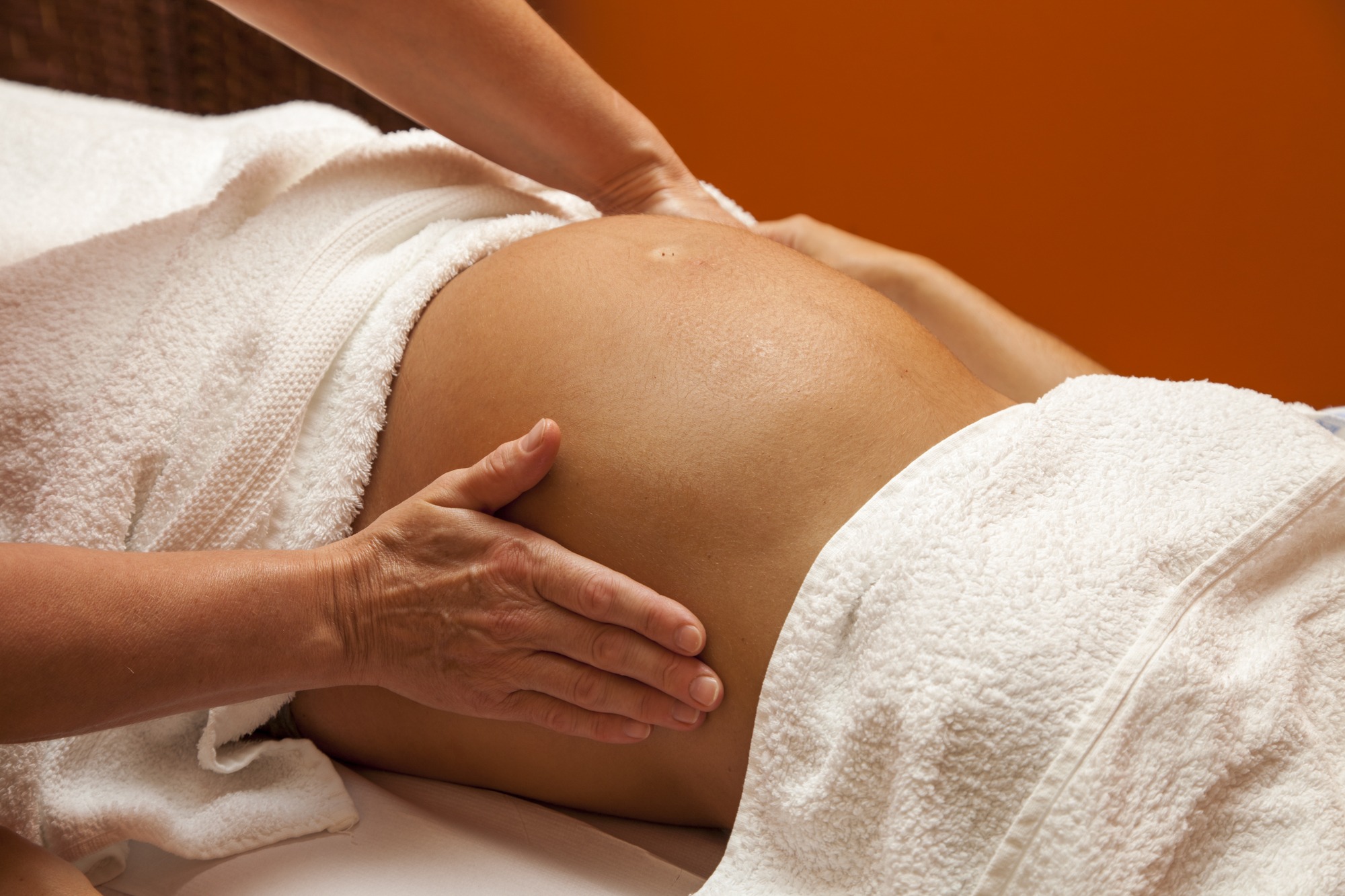 Pregnant young latina woman with beautiful skin, being wrapped with a towel, lying on a bed and having a relaxing prenatal massage, various techniques